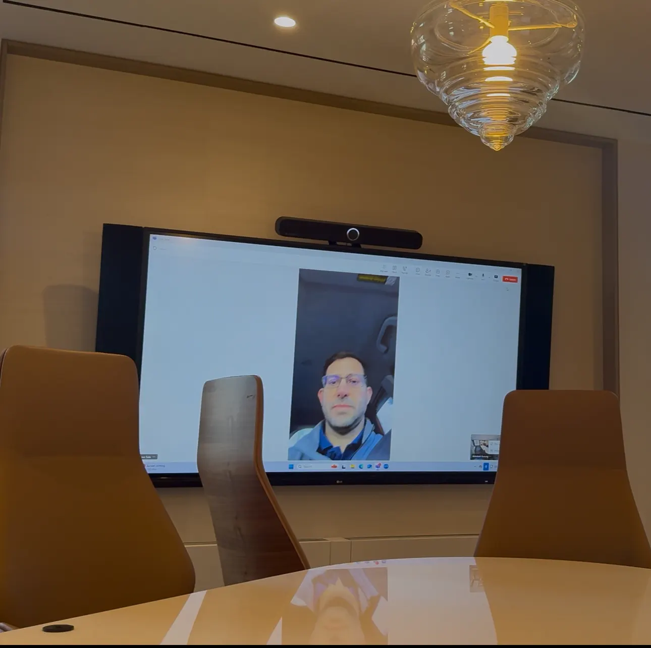 Meeting room display and video bar mounted on the wall facing a conference table